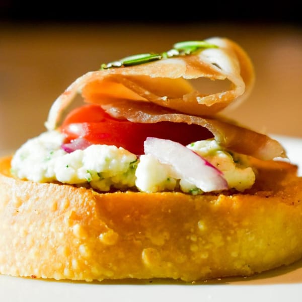 Italian bruschetta with ricotta, tomato, red onion, and prosciutto on toasted bread.
