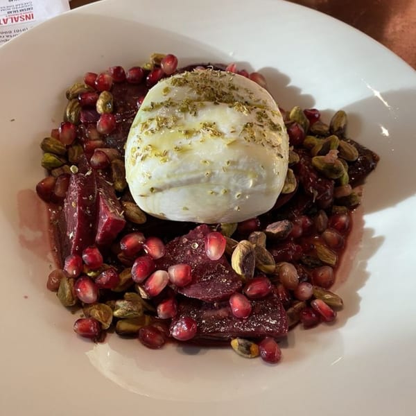 Burrata cheese with olive oil and herbs, surrounded by beets, pomegranate seeds, and pistachios.