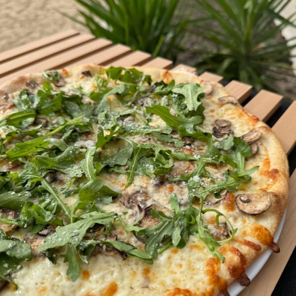 La Porta's mushroom and arugula pizza, topped with parmesan, on a wooden slatted table.