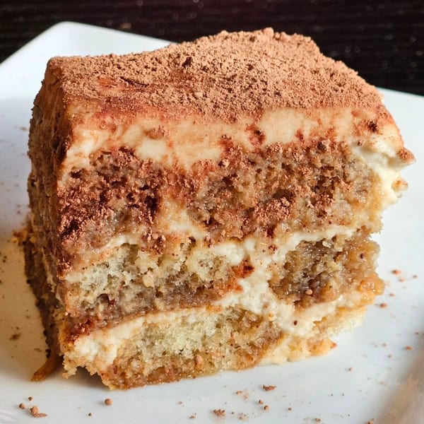 A close-up of a slice of tiramisu with visible layers of cake, cream, and cocoa powder.